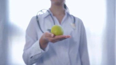 Ellerinde yeşil elma olan profesyonel diyetisyen, beyaz arka planda sağlıklı beslenmeyi tavsiye eden kameraya teslim oluyor.