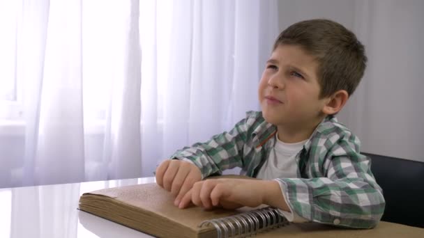 Сліпий хлопчик читає книгу брайля з символами шрифт для людей з вадами зору, що сидять за столом — стокове відео