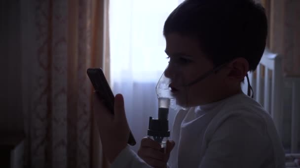 A gyermek egészségügyi ellátása, a beteg kisfiú mobiltelefont használ, miközben a légutak gyulladása gyógyszeres porlasztóval — Stock videók