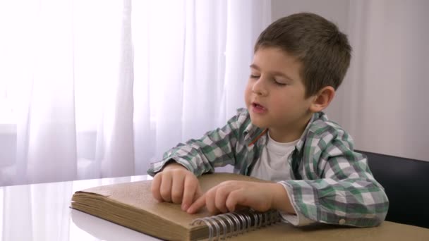 Обучение слепого, больного мальчика чтению книги Брайля с шрифтом символов для слабовидящих, сидящих за столом — стоковое видео