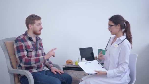 Portrait d'un médecin nutritionniste heureux, femme diététiste souriante fait un plan de régime pour le patient masculin pendant la consultation sur le bien-être et le poids santé et serrer la main tout en étant assis — Video