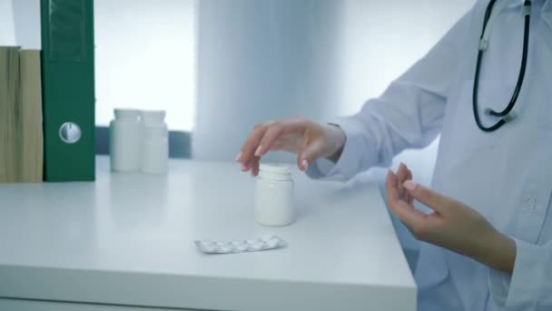 Doctor arms opens jar of nutritional supplements and pours yellow round pills into palm on white table — Stock Video