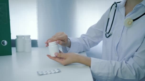Expert on food and health welfare opens jar of vitamins and pours yellow round pills into palm on white table — Stock Video