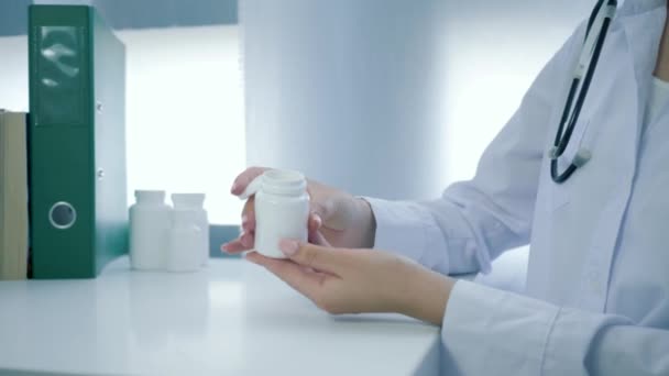 Медицинские руки открывает бутылку пищевых добавок и выливает желтые круглые таблетки в ладонь на белый стол — стоковое видео
