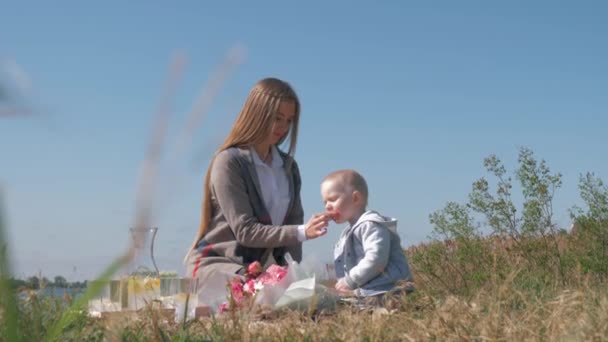 Jedzenie dla dzieci, młoda matka karmi małego chłopca czekoladą podczas rodzinnego pikniku na łonie natury — Wideo stockowe