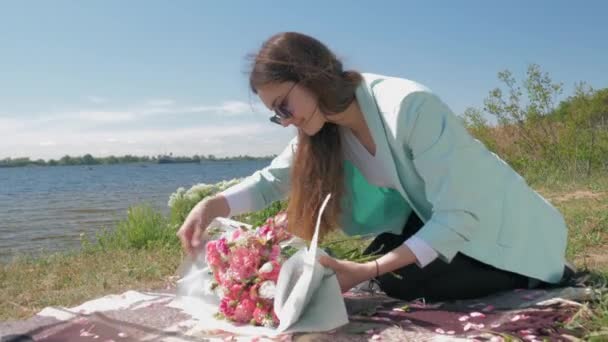 Virág, fiatal virágárus lány szemüvegben teszi gyönyörű csokor friss, szelíd virágok és csomagolási papír gyep közelében folyó — Stock videók