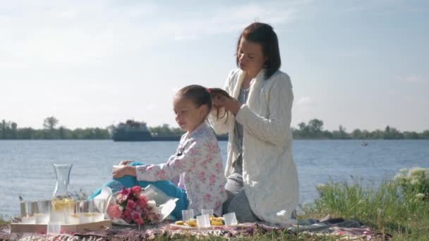 Mödravård, glad mamma gör dotter fläta under vila på familj picknick nära Loch — Stockvideo