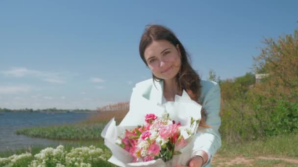 Sonriente dulce chica muestra hermoso ramo de flores en el césped en la naturaleza — Vídeo de stock