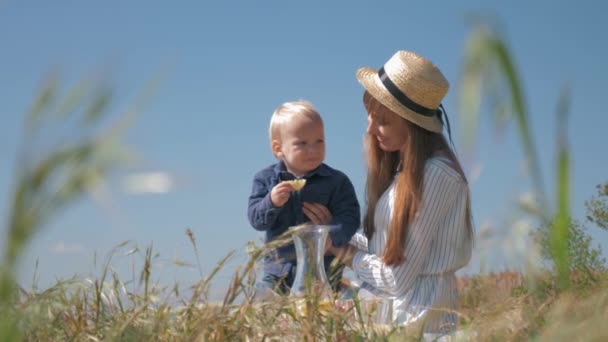 Сладкий малыш ест кислый лимон и гримасы во время семейного пикника на природе сидя рядом с мамой на руках в траве — стоковое видео