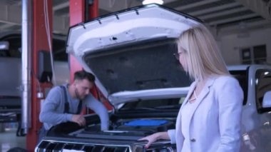 Benzin istasyonu, çalışan tamirci açık kaputlu aracı tamir ederken mutlu kadın tüketici araba sahibi portresi.