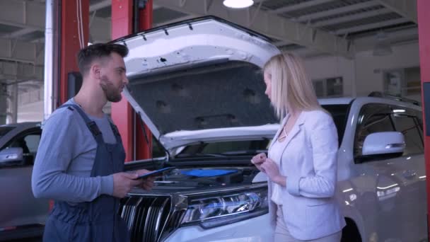 Otomobil servis merkezi, profesyonel tamirci servis atölyesinde kaputu açık ve el sıkışan bozuk araba hakkında müşteri kadına danışıyor. — Stok video