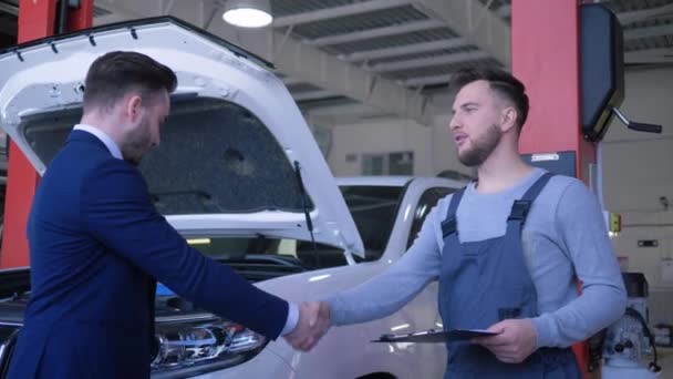 Auto service, konsumentens ägare lämnar över bilnycklar till mekaniker arbetare för professionell reparation och skakar hand nära maskin med öppen huva på bensinstation — Stockvideo