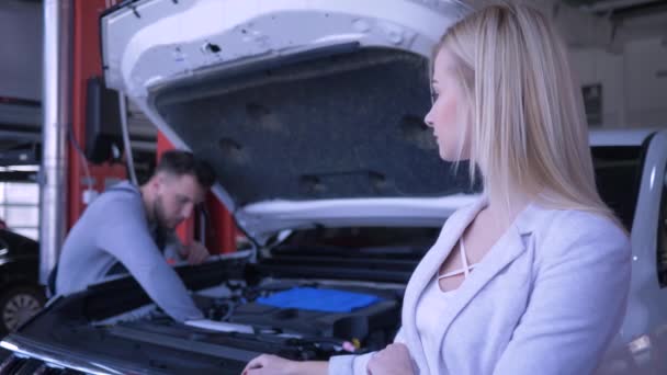 Ремонт автомобиля, несчастная клиентка женщина расстроена из-за сломанного автомобиля с открытым капюшоном, который ремонтируется техник в сервисном центре — стоковое видео