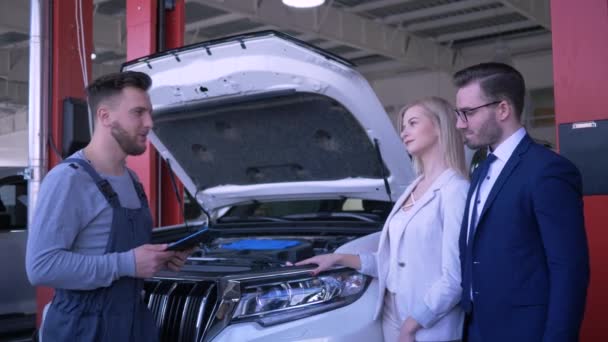 Kundservice i bilverkstad, professionell tekniker konsultera familjemedlem om trasiga bil med öppen huva efter reparation i bensinstation — Stockvideo
