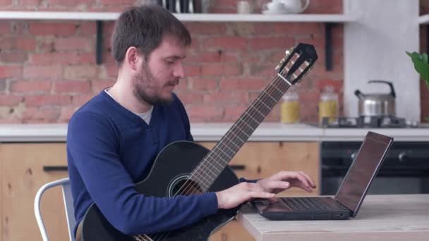 Neşeli müzisyen gitar çalma pratiği yapıyor çevrimiçi video eğitimi ve keyifli müzik içeren dizüstü bilgisayar kullanıyor. — Stok video