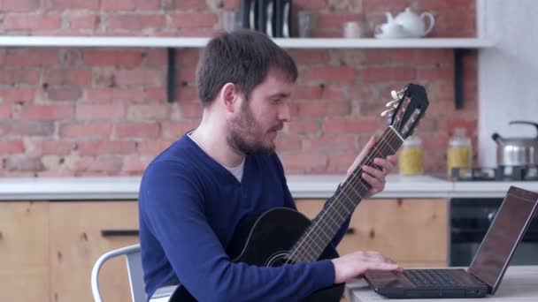 Музыкальное образование, смешной художник практикующий играть на гитаре использует ноутбук с онлайн видео учебник и насладиться музыкой — стоковое видео