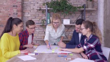 Başarılı iş anlaşmaları, neşeli ofis çalışanları ve kadınlar modern ofisteki çıkartmalı büyük kağıt üzerinde yeni bir proje kazanırken başparmak kaldırıyorlar.