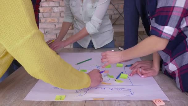 Креативна командна робота, руки офісних працівників крупним планом складають нову бізнес-ідею розвитку проекту на великому папері з наклейками за столом в сучасному офісі — стокове відео