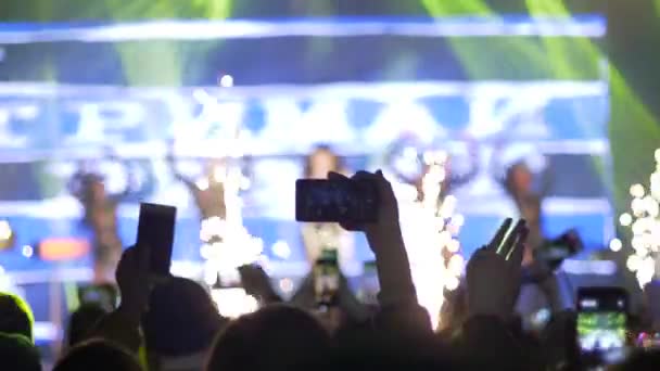 Руки болельщиков с мобильными телефонами делают фото- и видеозапись на рок-фестивале при свете сцены вечером — стоковое видео