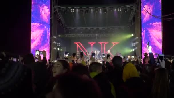 Болельщики толпы со смартфоном в руках получают удовольствие от живой музыки на рок-мероприятии в ярких огнях сцены вечером — стоковое видео