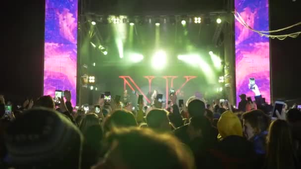 Menigte mensen met mobiele telefoons in handen genieten van live muziek op concert feest in helder podium schijnwerper in de nacht — Stockvideo