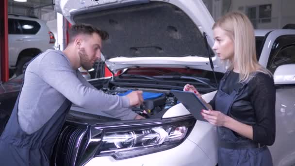 Manejo de automóviles, mecánica automotriz profesional hombre y mujer trabajando y hablando en la estación de servicio con la máquina de capucha abierta — Vídeos de Stock