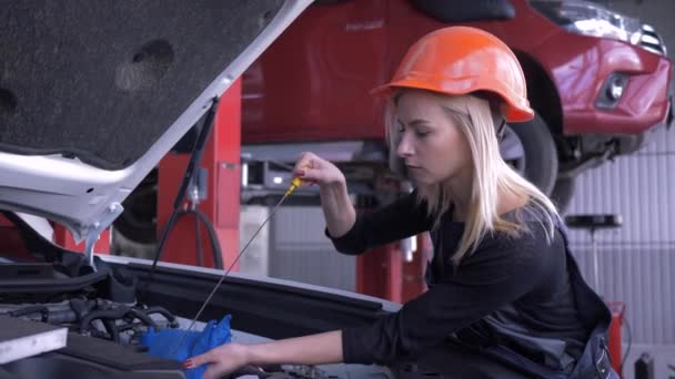 Car workshop, happy woman worker auto repairman checks oil level during automobile maintenance with open hood at service station and smiling — ストック動画