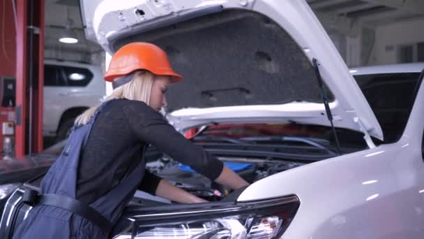 Портрет счастливой женщины-механика во время работы в автомастерской рядом с автомобилем с открытым капотом — стоковое видео