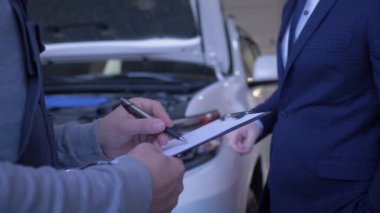 Otomobil teknisyeni, atölyede kaputu açık arabanın denetimi ve tamiri hakkında müşteriden ödev yazar.