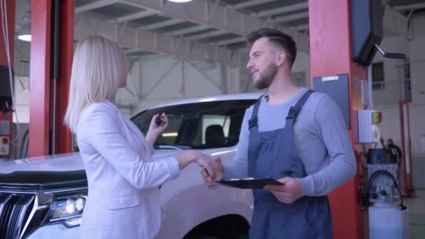 Otomobil servisi, araba sahibi tamir için araç anahtarlarını teknisyene verdi ve benzin istasyonunda otomobilin arka planında el sıkıştı. — Stok video