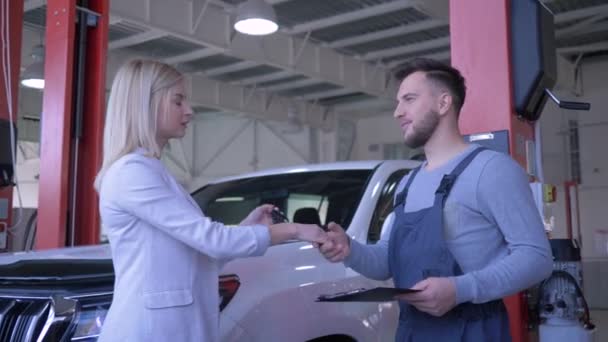Araba servisi, müşteri bayan tamir için araba tamircisinin anahtarlarını verdi ve servis atölyesinde arka plan makinesinde el sıkıştı — Stok video