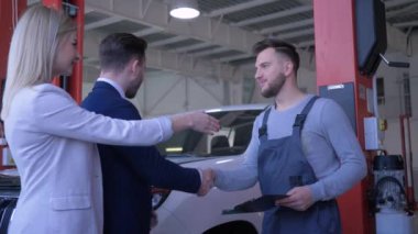 Genç çift müşterileri otomobil tamircisine araba bakımı hakkında danışmanlık yapıyor ve benzin istasyonundaki tablete ödev yazıyorlar