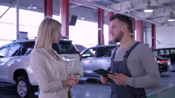 Service station, happy client girl and mechanic talking about car maintenance at auto repair shop — Stock Video