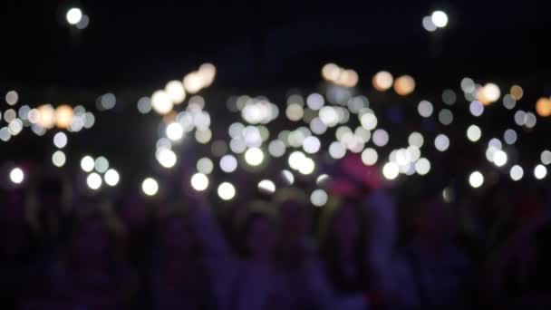 Manos de los fans con smartphone con linternas encendidas ondeando en concierto de rock nocturno en desenfocado — Vídeo de stock