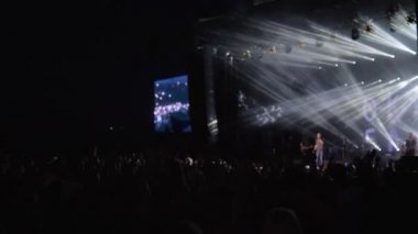 Kalabalık taraftarları rock canlı müzik partisinde büyük ekranlı parlak sahne karşısında el çırpıyor.