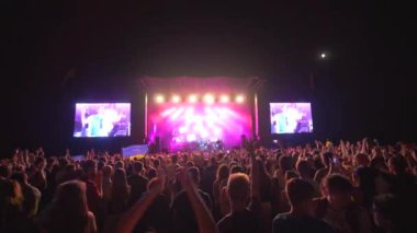Rock festivali, birçok hayran alkışlıyor ve canlı müzik konserinde büyük ekranlı sahneye el sallıyor.