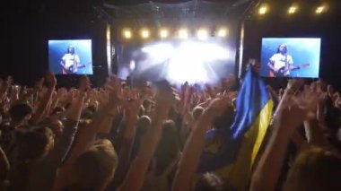 Rock partisi, kalabalık hayranları canlı müzik konseri için el sallıyor. Gecenin karanlığında büyük ekranlarla aydınlık sahneye karşı.