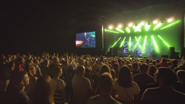 Menigte fans klappen handen op rock live muziek concert tegen fel verlichte scène met grote schermen 's nachts — Stockvideo