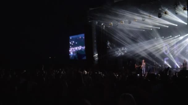 Multitud fans aplauden de la mano en la fiesta de música rock en vivo contra la escena brillantemente iluminada con pantallas grandes en la noche — Vídeos de Stock