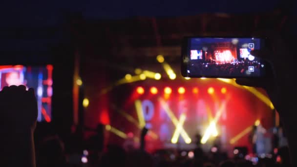 Fans met mobiele telefoons in handen genieten van live muziek op rockconcert in heldere scène lichten in de avond — Stockvideo