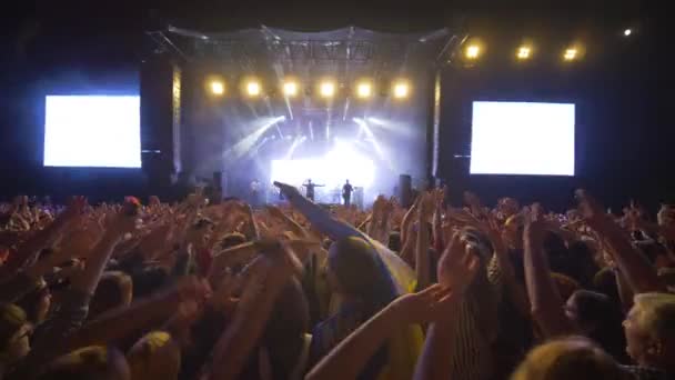 Live muziekconcert, veel fans zwaaien handen op rockfestival tegen fel verlichte podium met grote schermen 's nachts — Stockvideo