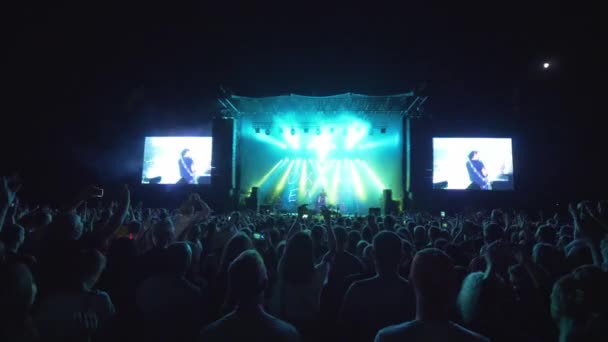 Veel fans klappen handen op rock live muziekfestival tegen fel verlichte scène met grote schermen 's nachts — Stockvideo