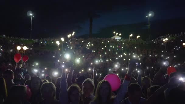 Festival ao ar livre, fãs de multidão com lanternas no smartphone acenando as mãos e desfrutar de música ao vivo durante o concerto noturno ao ar livre — Vídeo de Stock