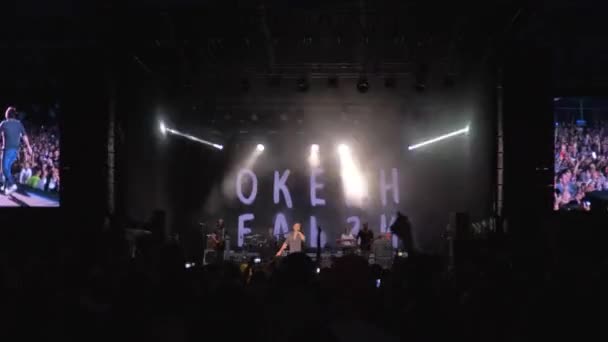 Rock artysta występuje na scenie przed tłumem fanów na nocnym koncercie muzycznym na oświetlonej scenie z dużymi ekranami i jasnymi reflektorami — Wideo stockowe