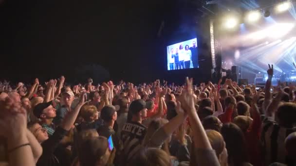 Rock esemény, tömeg fiatalok tapsolnak élő zenei koncert ellen fényes színpadon nagy képernyők éjjel Sötétben — Stock videók