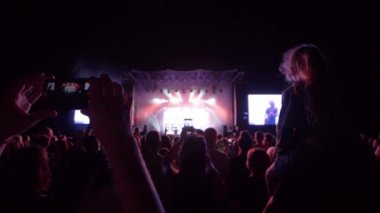 Kişi silueti, gece saatlerinde rock konserinde arka plandaki kalabalıktan cep telefonuna video kaydediyor.