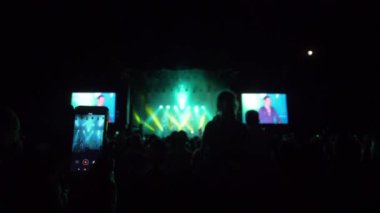 Akıllı telefonlu hayranlar, arka plandaki kalabalığın video kaydına gece vakti rock festivalinin parlak sahne ışıklarıyla dalıyorlar.