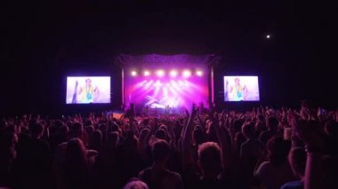 Canlı müzik, birçok hayranı ritme atlıyor ve gece büyük ekranlı parlak sahne karşısında rock konserinin keyfini çıkarırken el çırpıyor.