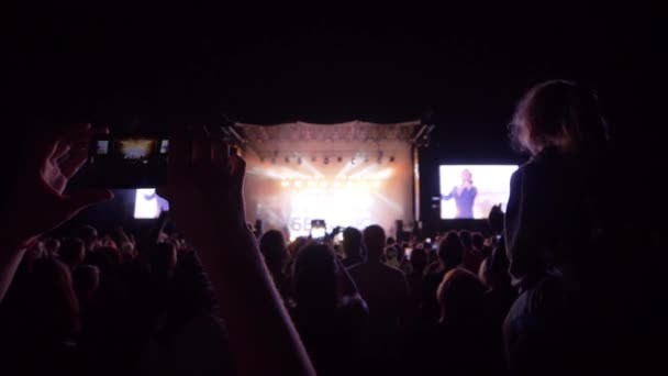 Nachtleven, veel mensen met mobiele telefoons in de armen bij rockconcert in zoeklicht — Stockvideo