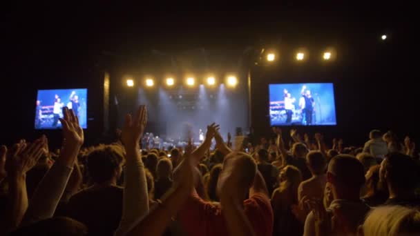 Рок-фестиваль, багато шанувальників плескають в долоні і насолоджуються музикою на концертах у яскраво освітлених сценах у повільному русі. — стокове відео